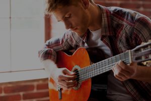 Homem tocando violão com os olhos fechados