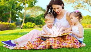 Mães lendo livro com os filhos sentada na grama